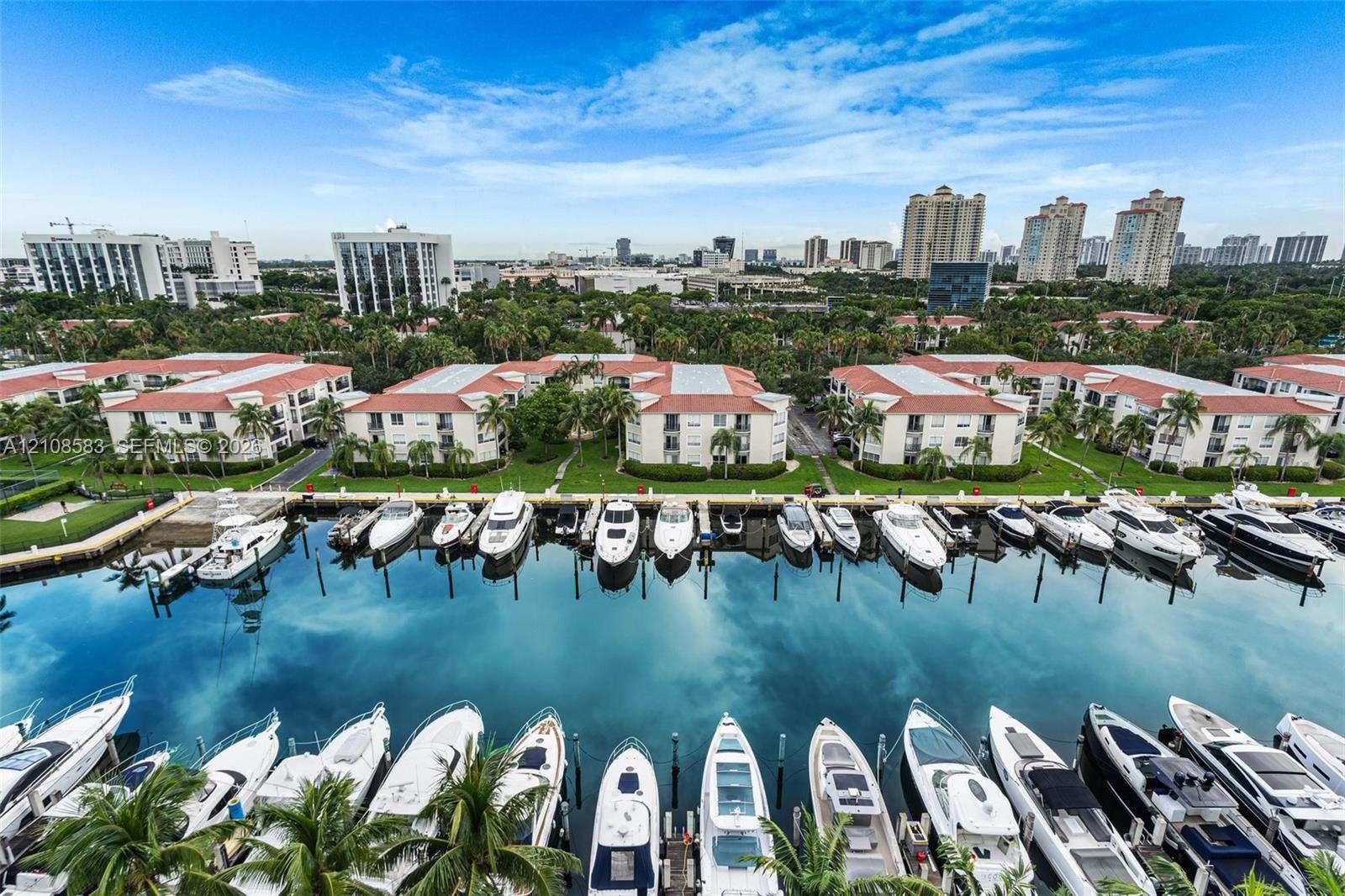 Waterfront complex featuring a private deep-water marina with boat slips, multi-story stucco buildings with tile roofs, and expansive community green spaces