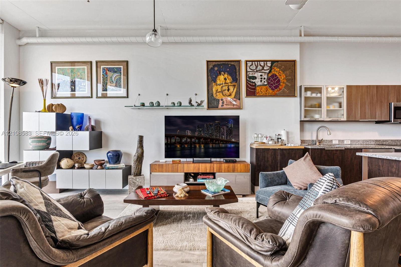 Open-concept interior featuring exposed industrial piping, flat-panel cabinetry with glass-front uppers, and solid-surface countertops Open-concept interior featuring exposed industrial piping, flat-panel cabinetry with glass-front uppers, and solid-surface countertops