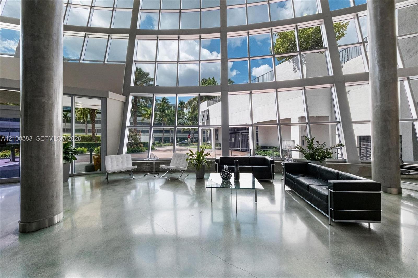 Grand two-story floor-to-ceiling glass wall, polished concrete flooring, and cylindrical structural columns