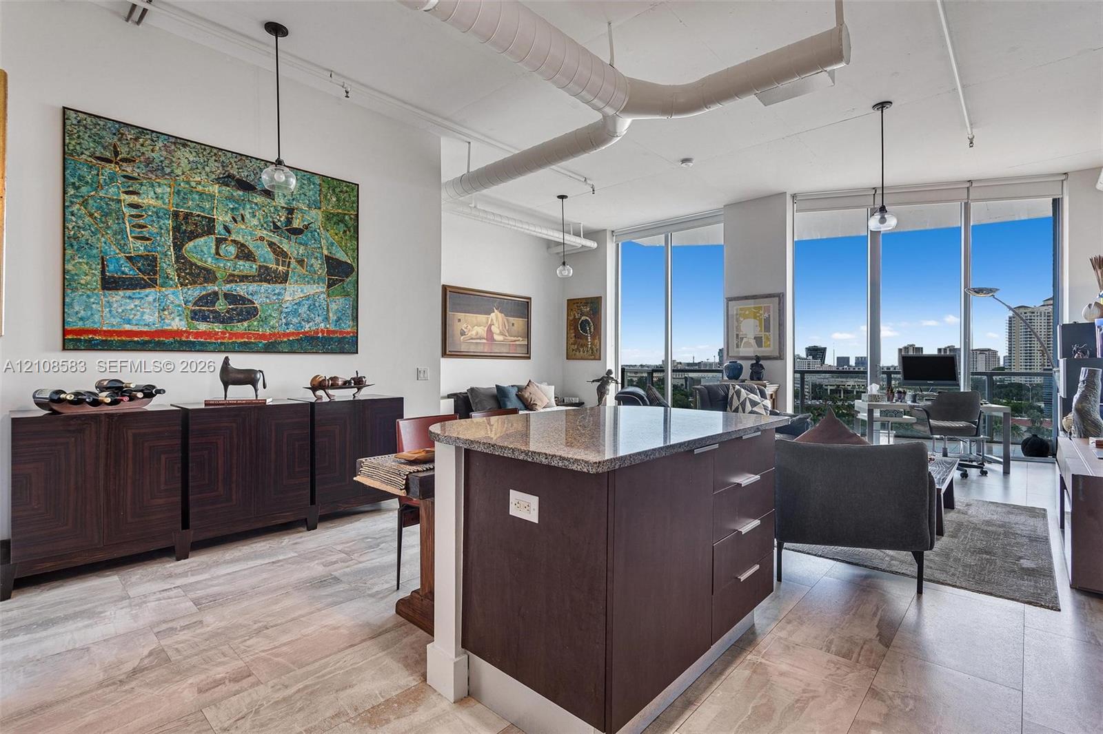 Open-concept interior featuring floor-to-ceiling windows, exposed industrial ductwork, polished stone tile flooring, and a kitchen island with stone countertop and dark cabinetry