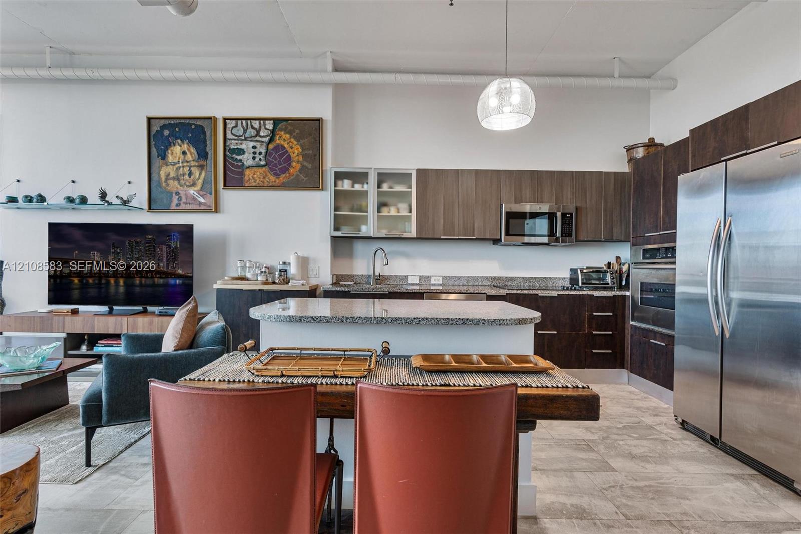 Kitchen featuring dark wood-finish cabinetry, stone countertops, stainless steel appliances, a center island with integrated dining surface, and large-format tile flooring
