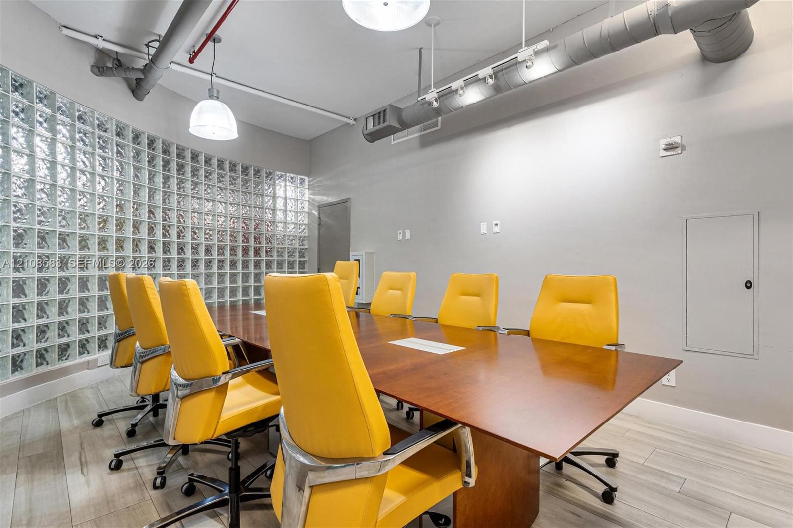 Interior space featuring a glass block wall, wood-finish flooring, exposed industrial ductwork, and pendant lighting