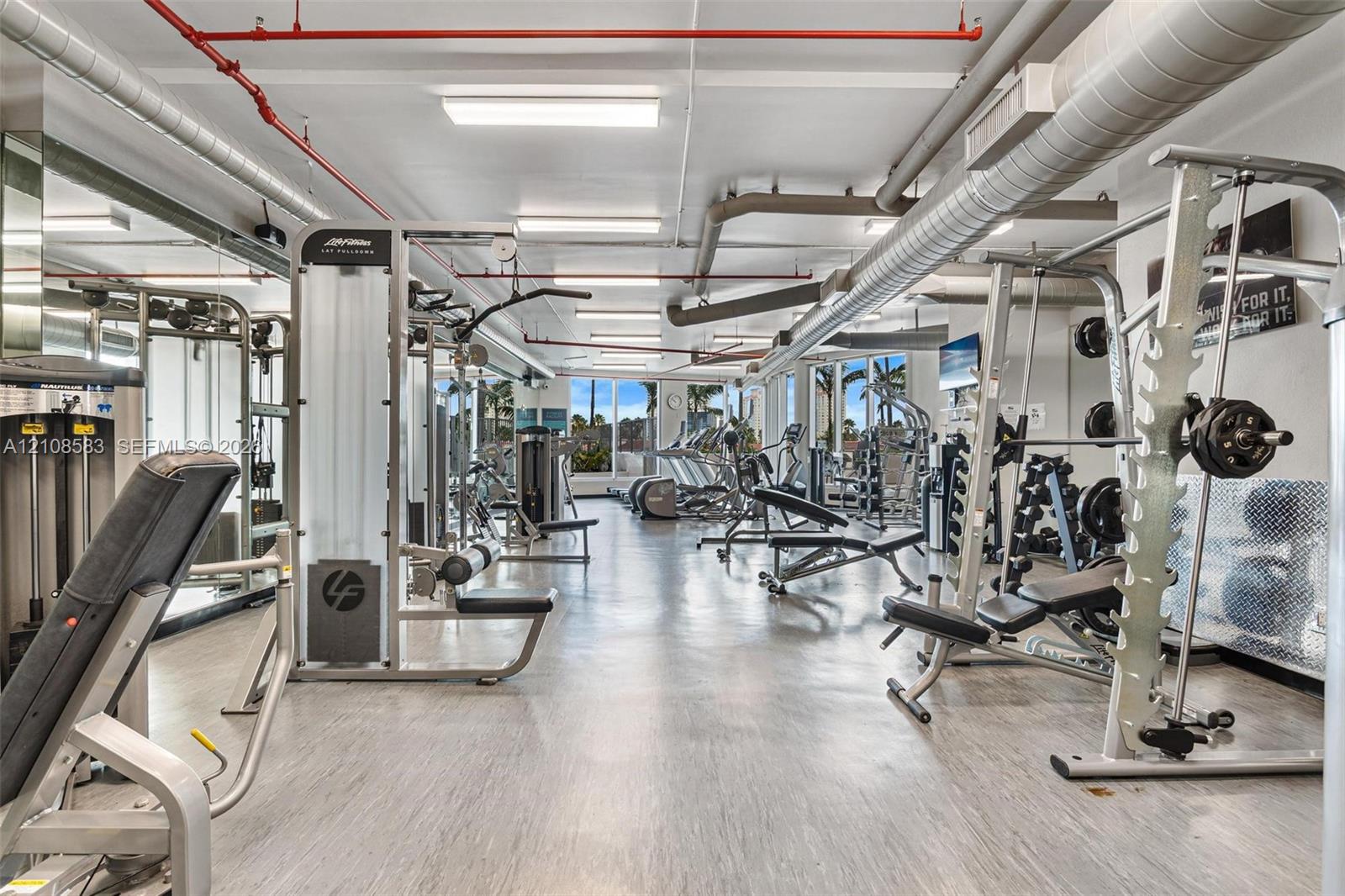 Fitness center featuring industrial-style exposed ductwork, large-format tile flooring, recessed overhead lighting, and floor-to-ceiling windows