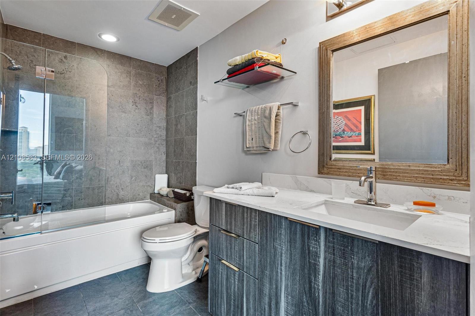Bathroom featuring a vanity with dark wood-finish cabinetry, white countertop, integrated rectangular sink, wall-mounted faucet, and a tiled shower enclosure with a glass panel
