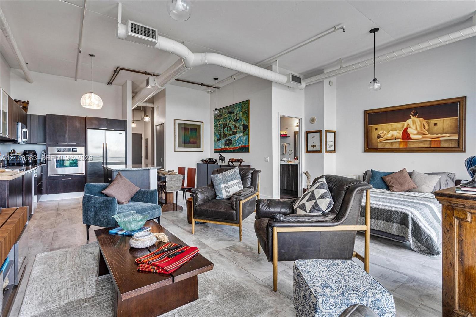 Open-concept industrial-style interior featuring high ceilings with exposed ductwork, dark-finish cabinetry, built-in stainless steel appliances, and large-format tile flooring Open-concept industrial-style interior featuring high ceilings with exposed ductwork, dark-finish cabinetry, built-in stainless steel appliances, and large-format tile flooring