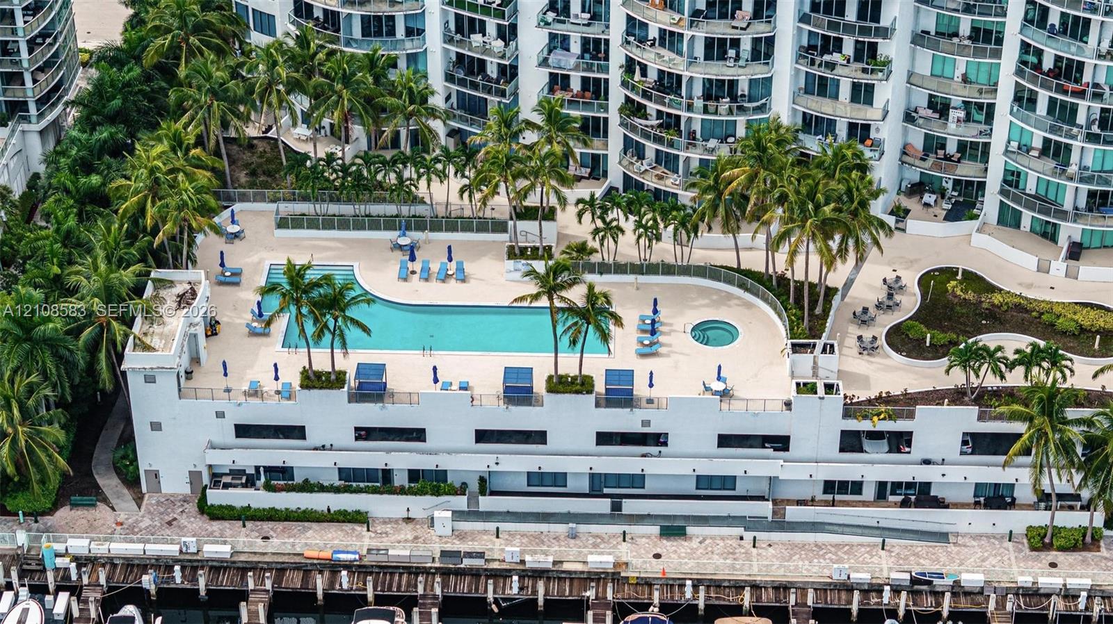 Swimming pool and integrated spa on a tiled terrace, featuring palms, paved landscaping, and direct water frontage