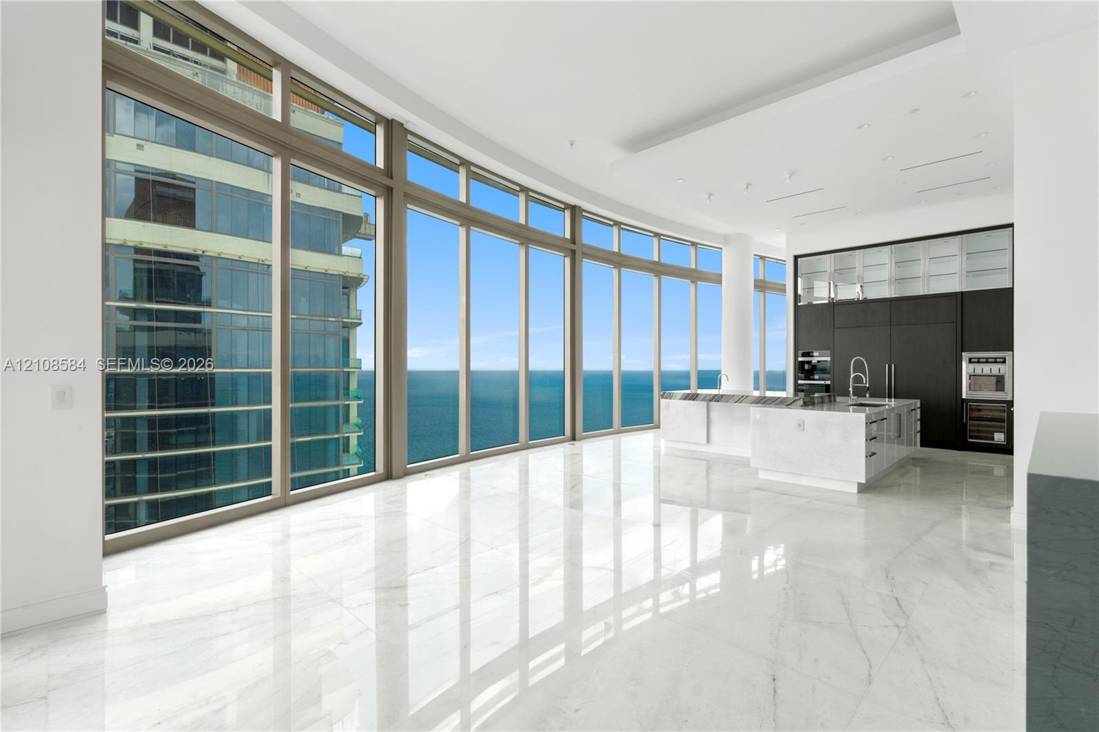 Floor-to-ceiling windows featuring panoramic water scenery, polished stone flooring, custom dark cabinetry, stone-topped kitchen island, and built-in stainless steel appliances
