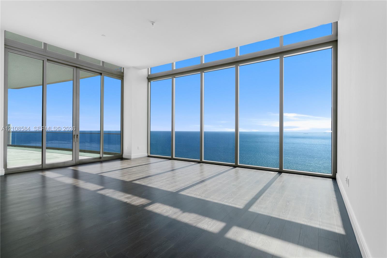 Floor-to-ceiling windows, wood-finish flooring, sliding glass doors, and a glass-paneled balcony