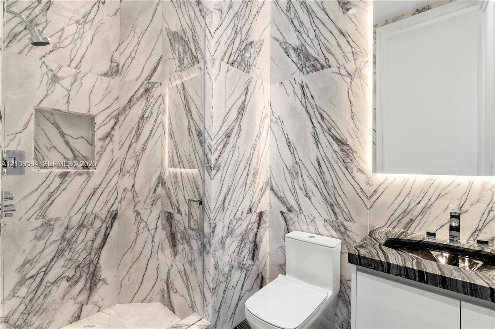 Shower enclosure featuring floor-to-ceiling veined stone tile, a built-in recessed niche, and a glass partition