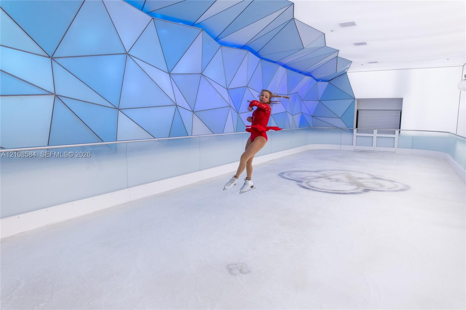 Indoor ice rink featuring a geometric patterned wall installation, high-gloss ice surface, and glass panel perimeter railing