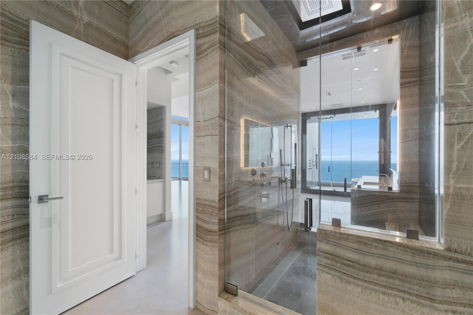 Floor-to-ceiling stone wall cladding, walk-in glass-enclosed shower with wall-mounted fixtures, and recessed ceiling lighting