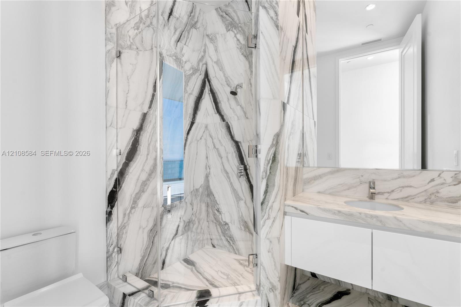 Full-height stone wall tiling, glass-enclosed shower, wall-mounted floating vanity, integrated countertop with oval basin, and expansive wall-mounted mirror