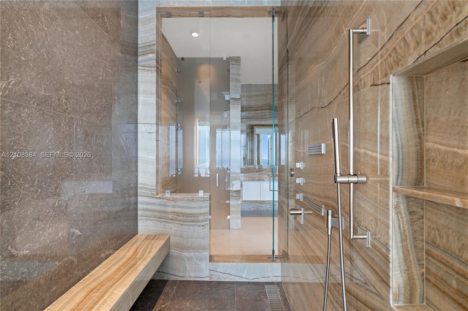 Walk-in shower featuring slab wall tile, a built-in stone bench, glass enclosure, recessed wall niche, and polished metal fixtures