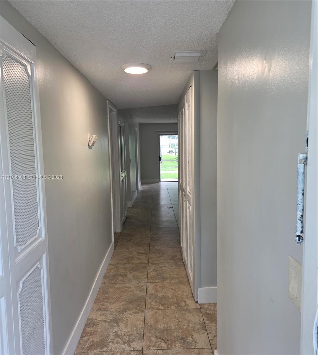 Hallway featuring large-format ceramic tile flooring, built-in floor-to-ceiling storage cabinetry with louvered doors, and flush-mount ceiling lighting