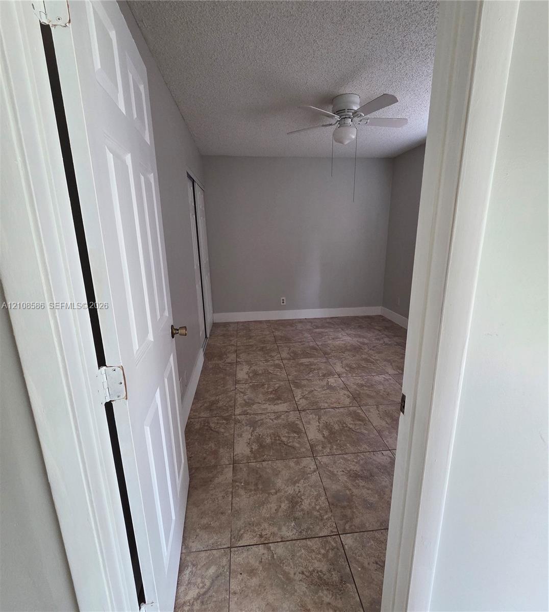 Neutral-toned interior space featuring stone-style tile flooring, white six-panel doors, and a ceiling-mounted light fixture with integrated fan