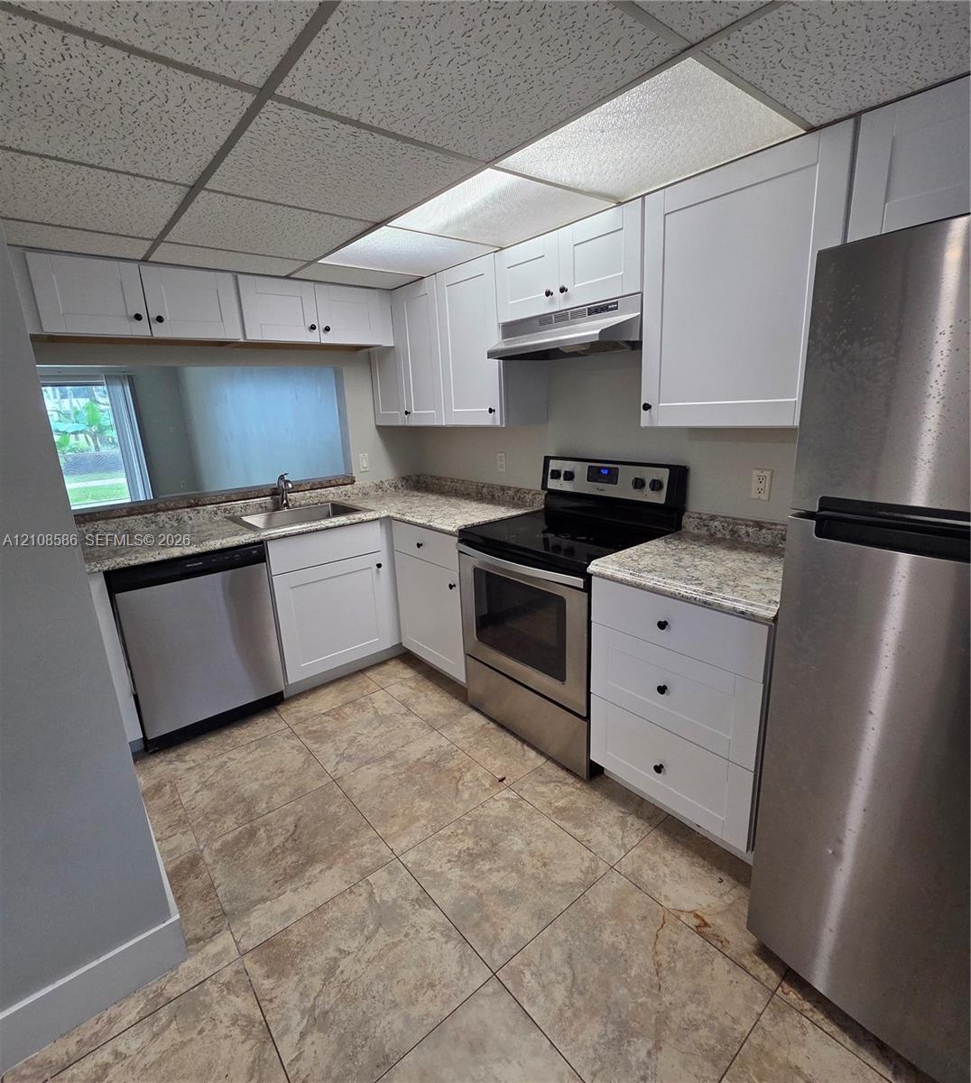 Kitchen featuring white shaker-style cabinetry, stone-patterned countertops, stainless steel appliances, and tile flooring