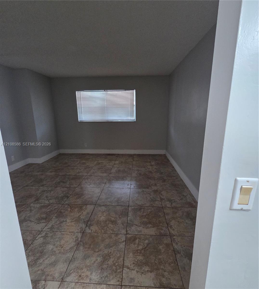 Interior space featuring neutral wall paint, large-format tile flooring, and a window with integrated blinds