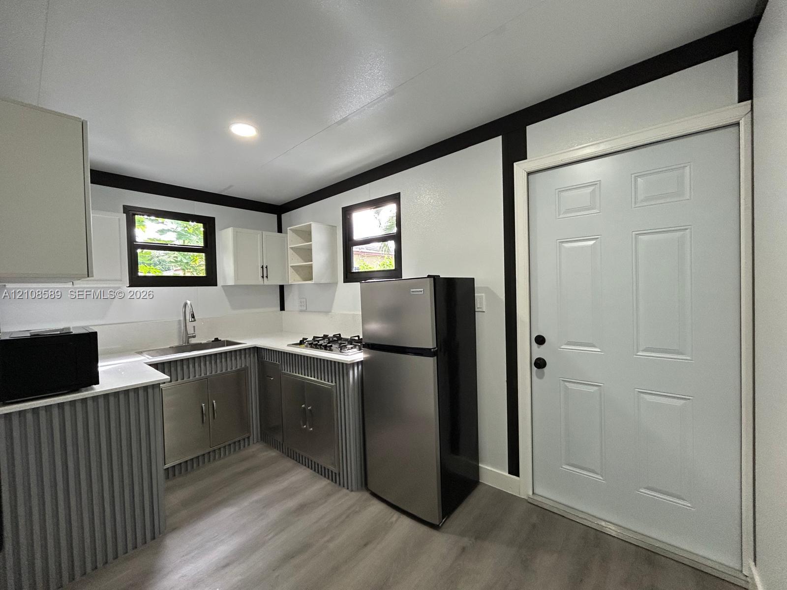 Kitchen featuring metal corrugated cabinetry, white solid-surface countertops, wood-finish flooring, and recessed ceiling lighting