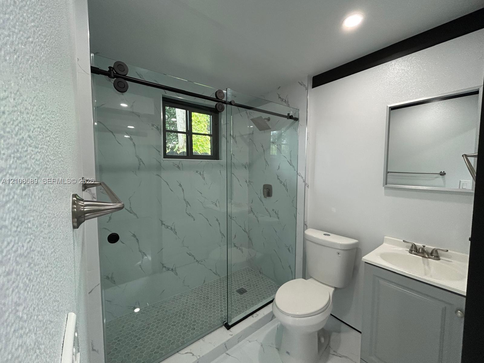 Walk-in shower featuring glass sliding doors, stone-patterned wall tile, and hexagonal floor tile, paired with a vanity featuring a drop-in sink and a framed mirror