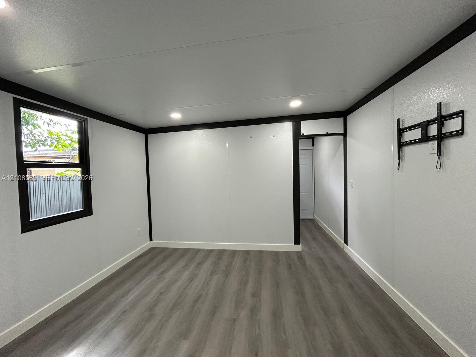 Interior room featuring wood-finish flooring, high-contrast black trim, recessed lighting, and a single-pane window