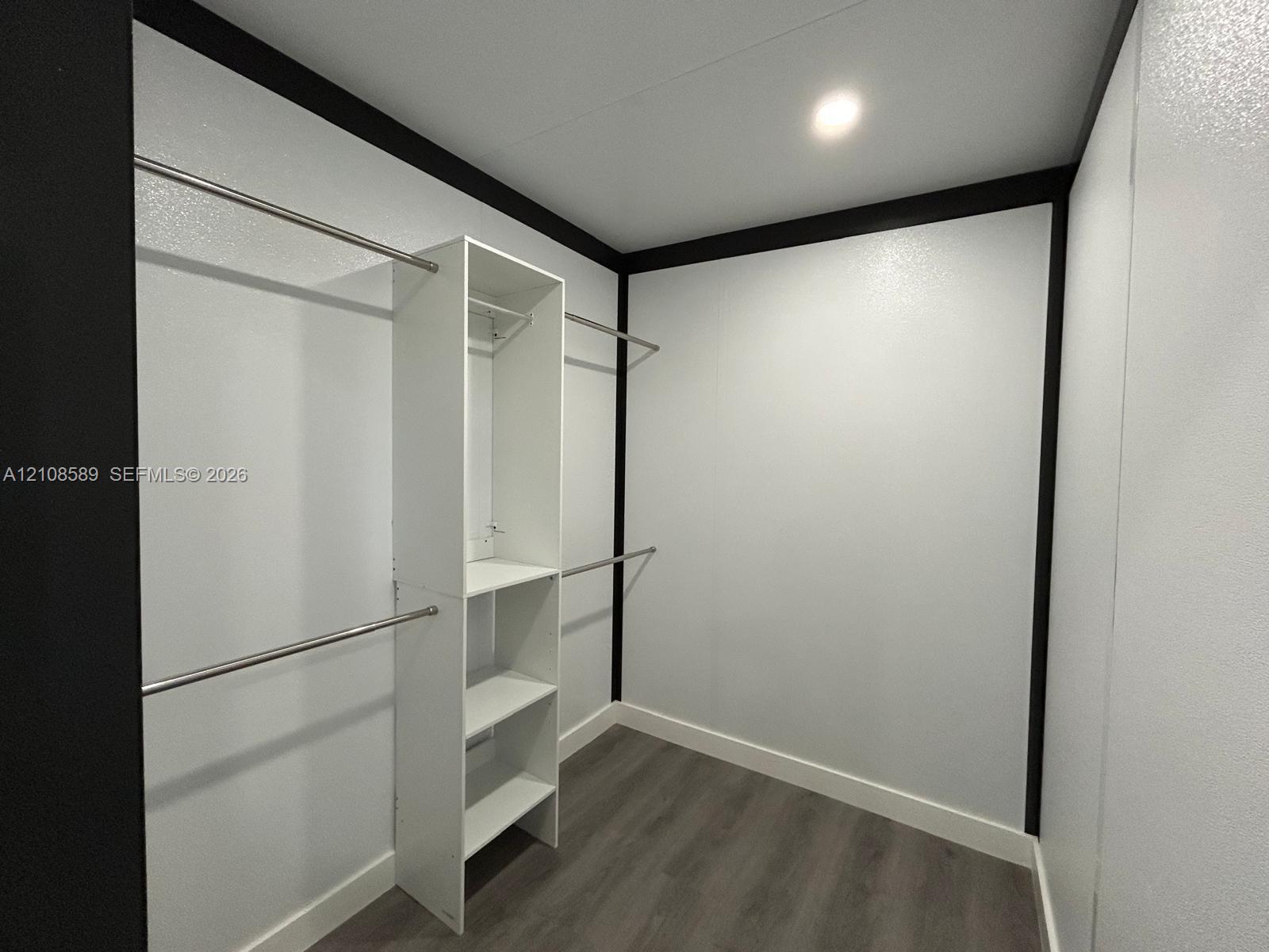 Walk-in closet featuring white built-in shelving, dual-level metal hanging rods, wood-finish flooring, and high-contrast trim