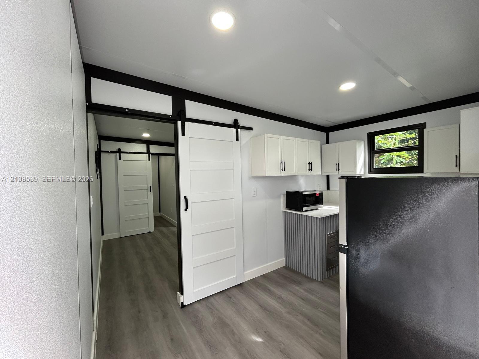 Interior space featuring white shaker-style cabinetry, wood-finish flooring, high-contrast black trim, and sliding barn doors with matte black hardware