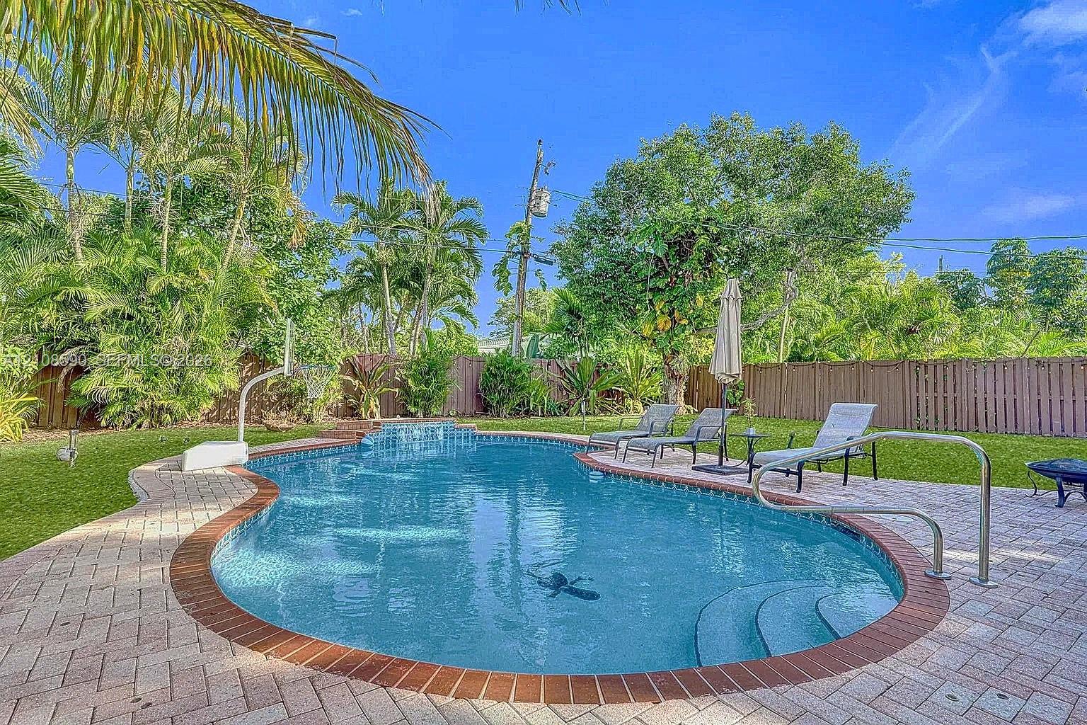 In-ground swimming pool featuring a brick paver surround, integrated entry steps, and metal handrails, complemented by a grass lawn and privacy fencing