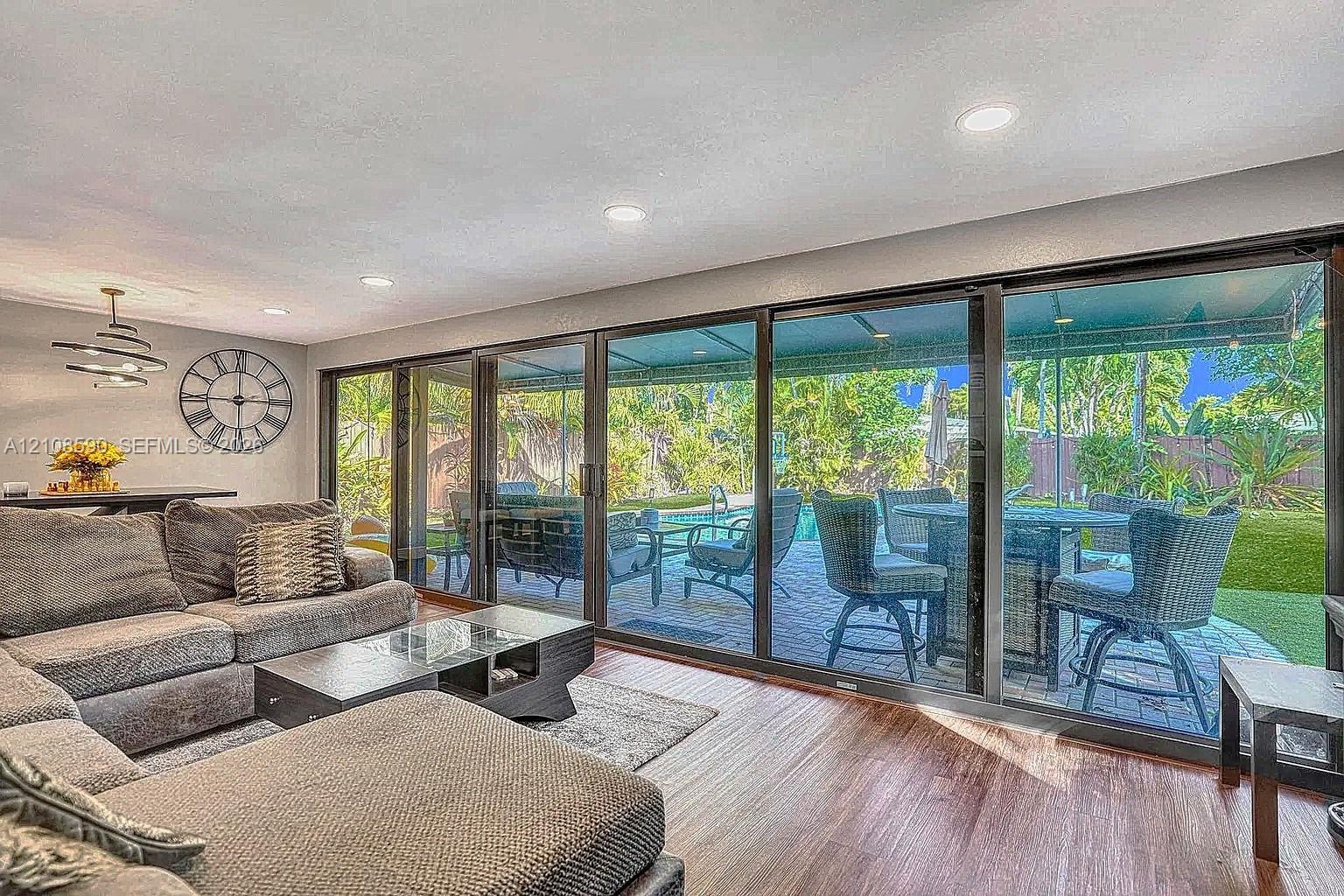 Full-height sliding glass doors featuring dark frames, wood-finish flooring, recessed lighting, and a modern multi-tier chandelier