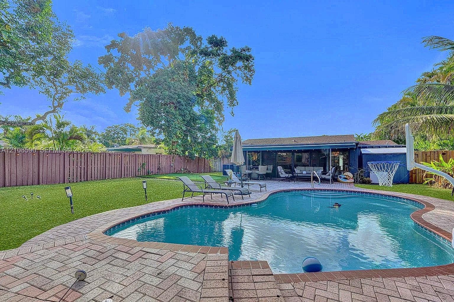 Backyard featuring a swimming pool, brick paver decking, manicured lawn, and perimeter wood fencing
