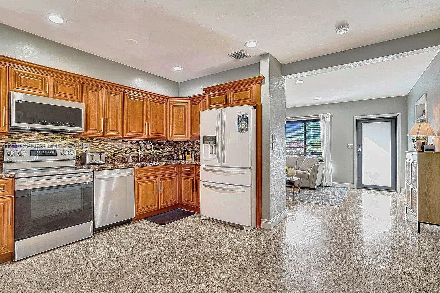 Kitchen featuring wood cabinetry, stainless steel appliances, decorative stone-patterned backsplash, and polished hard-surface flooring with recessed lighting