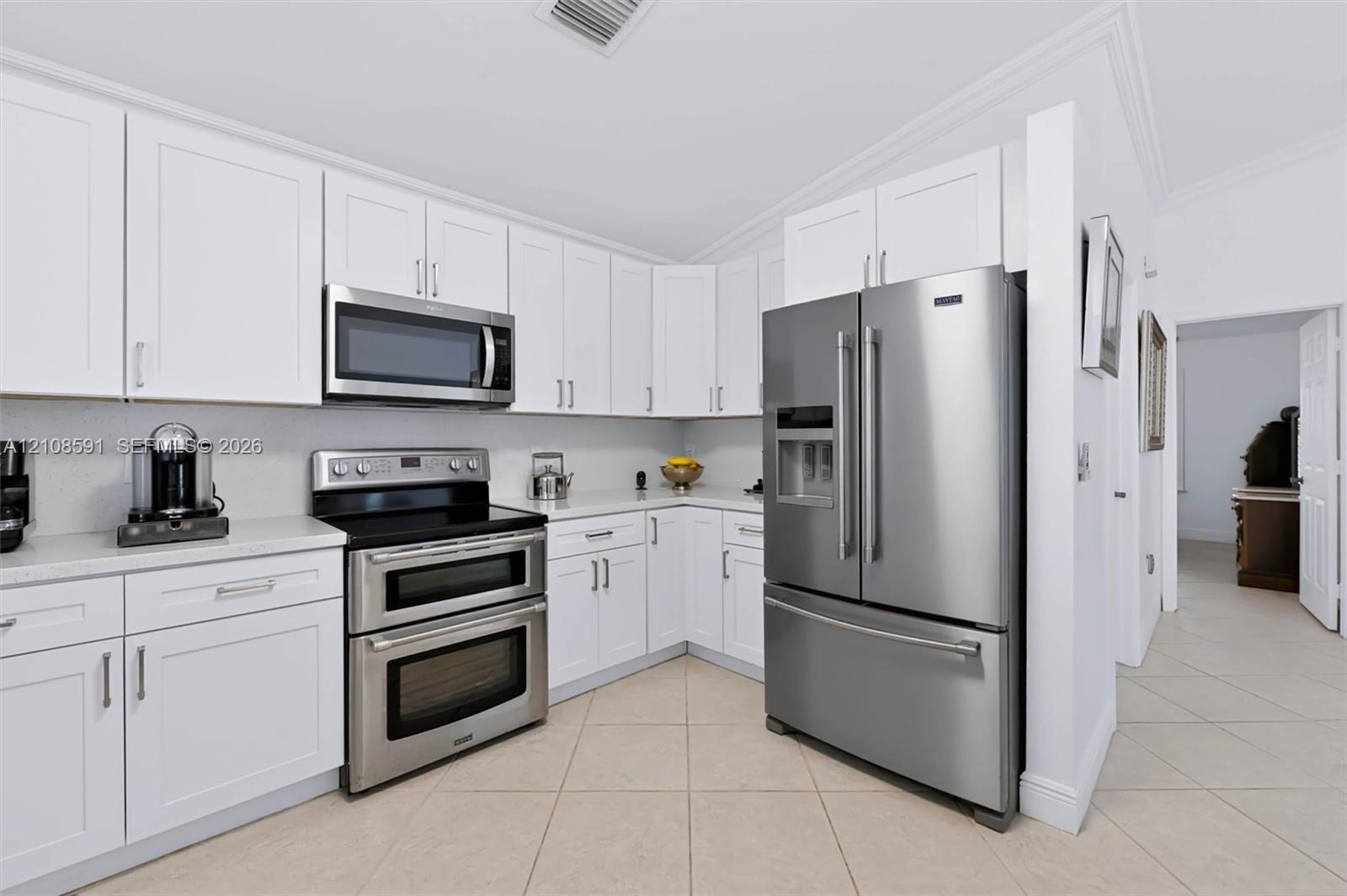 Kitchen featuring white shaker-style cabinetry, solid-surface countertops, and stainless steel appliances including a dual-oven range, built-in microwave, and French-door refrigerator