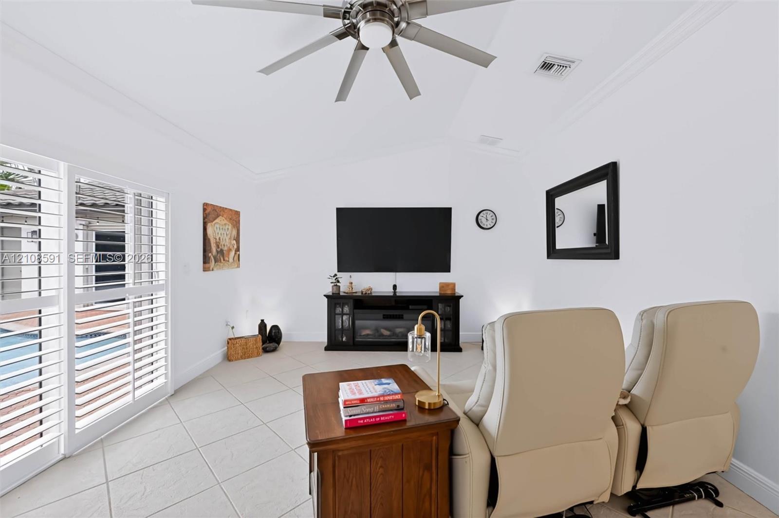Vaulted ceiling with a central brushed-nickel ceiling fan, large-format tile flooring, and sliding glass doors featuring white plantation shutters