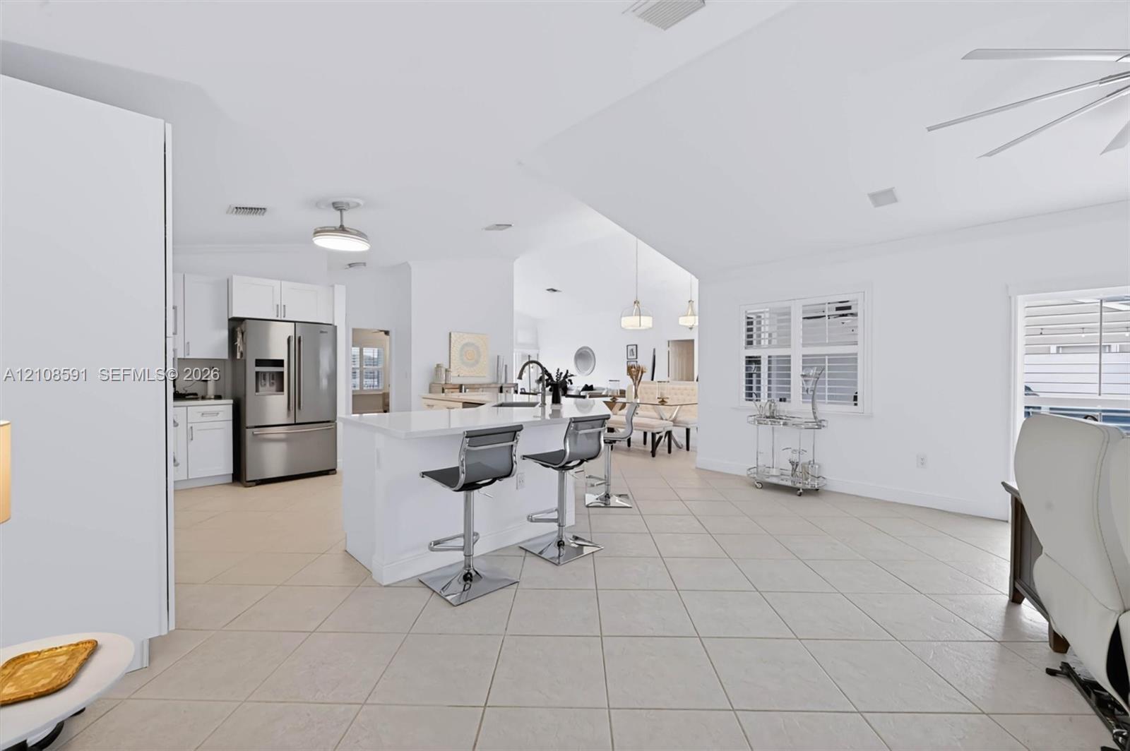 Open-concept kitchen featuring white shaker-style cabinetry, quartz countertops, a central island, tile flooring, and vaulted ceilings