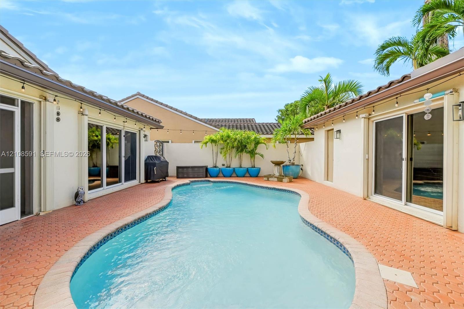 Enclosed courtyard featuring a swimming pool, terracotta-style paved patio, white perimeter wall, and sliding glass door access