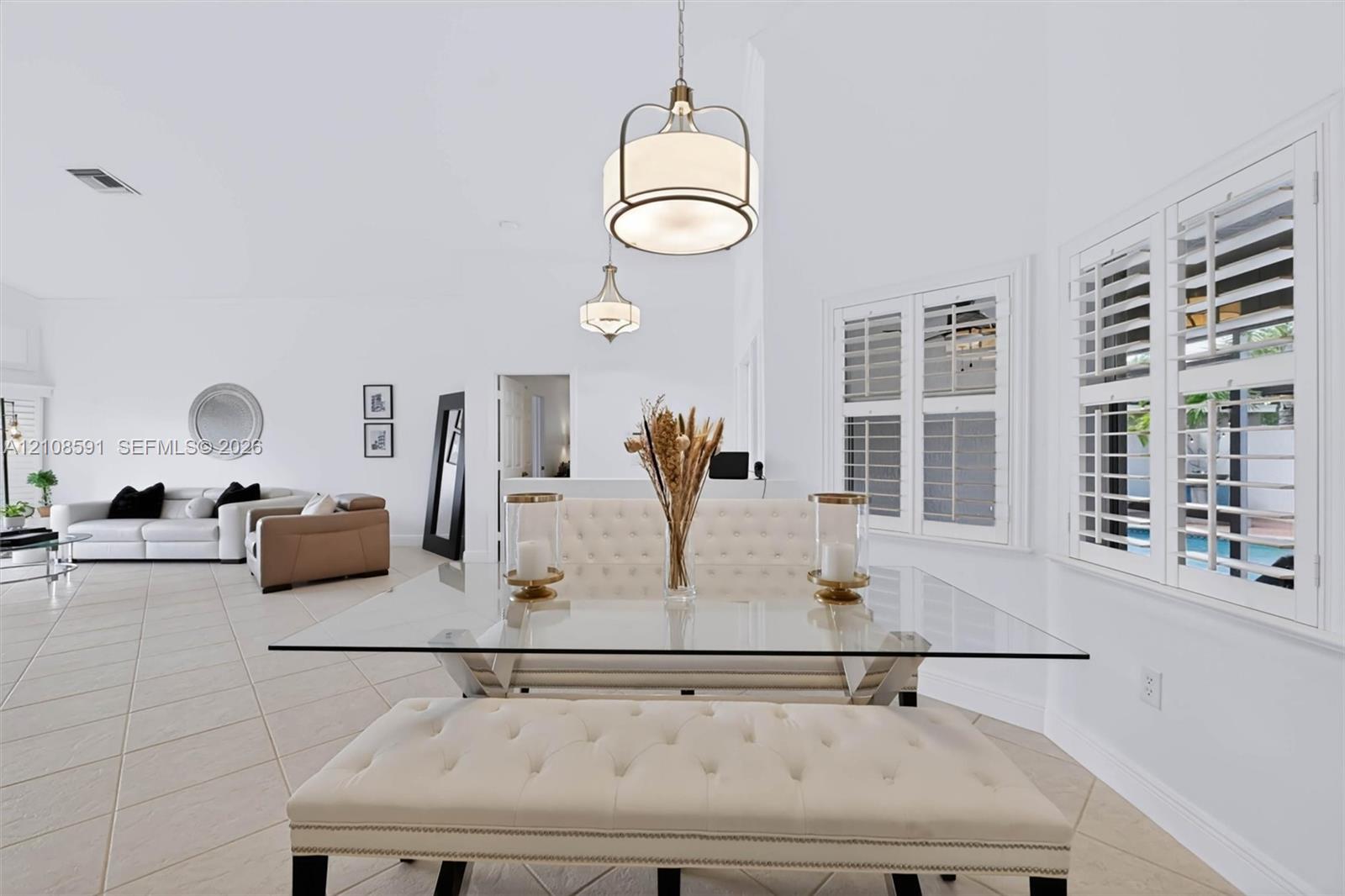 High-ceilinged room featuring large-format ceramic tile flooring, dual drum-style pendant light fixtures, and white plantation shutters