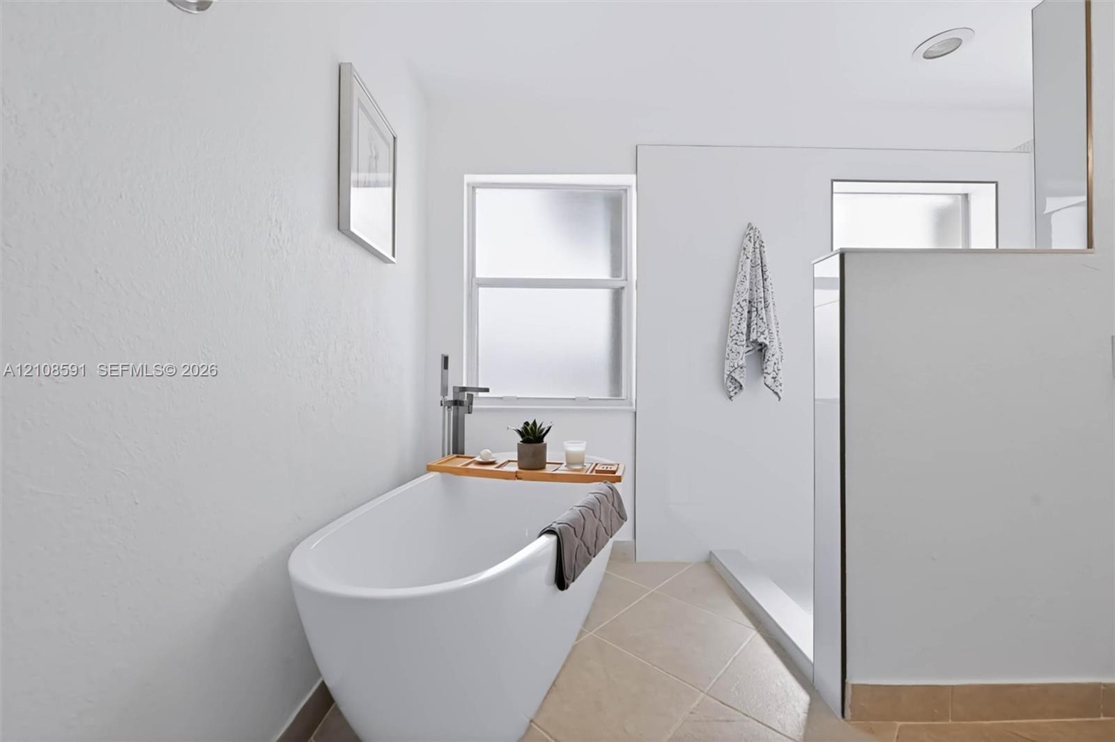 Freestanding soaking tub with a floor-mounted faucet, walk-in shower enclosure, and neutral tile flooring