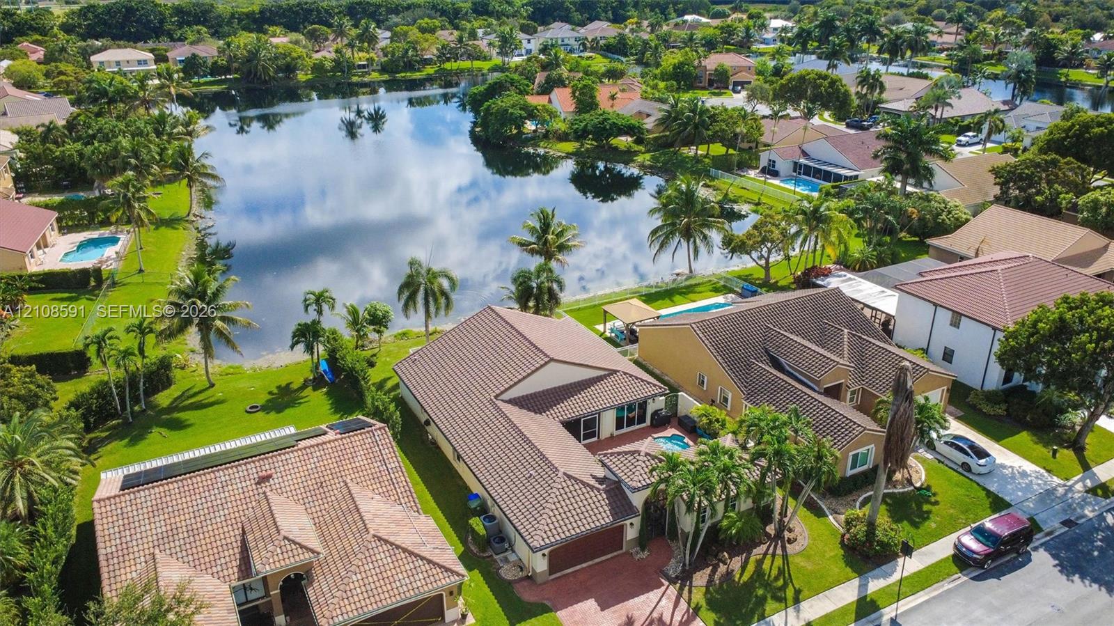 Aerial perspective featuring a tile roof, paved driveway, swimming pool, and direct lake frontage