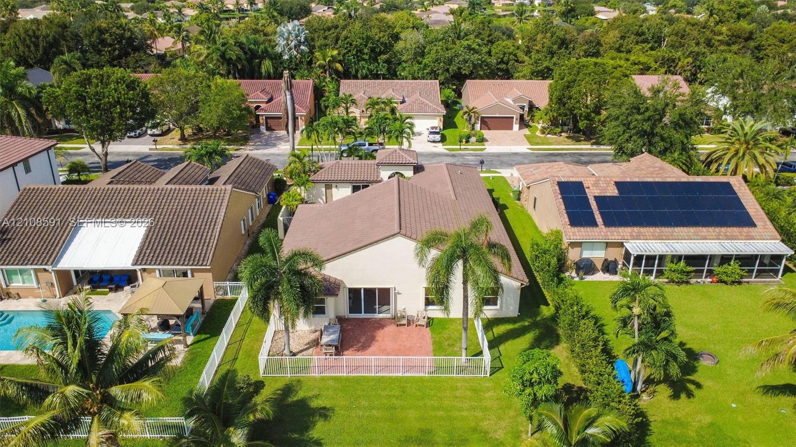 Aerial perspective featuring a neutral-toned stucco exterior, a multi-pitched roof, a paved patio, and a fenced yard with mature landscaping