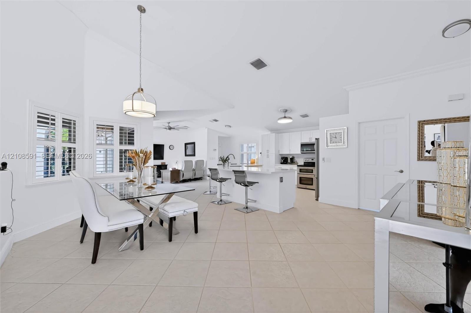 Open-concept interior featuring vaulted ceilings, tile flooring, a kitchen island with stone-finish countertops, crisp white cabinetry, and plantation shutters