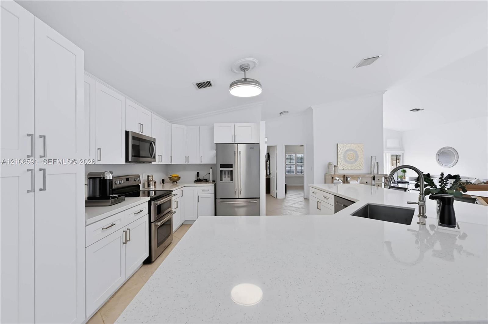 Kitchen featuring white shaker-style cabinetry, a quartz countertop island with an undermount sink, stainless steel appliances, and a modern ceiling-mounted light fixture