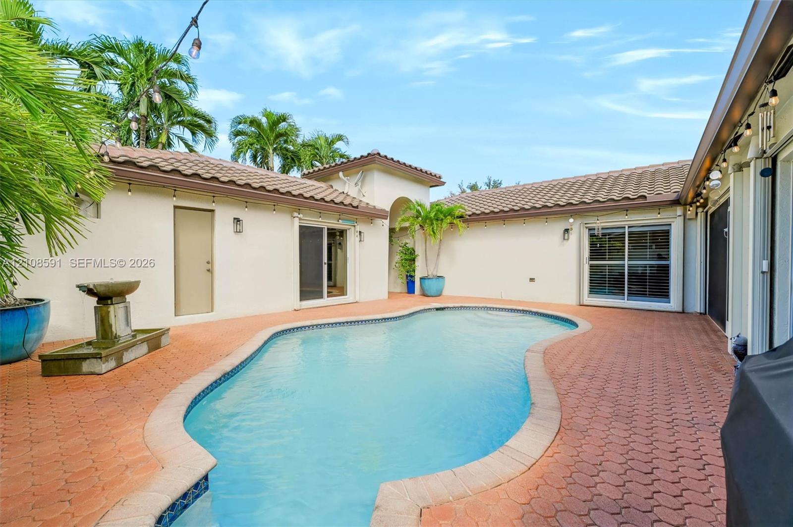 Courtyard pool featuring paved hardscaping, stucco exterior, clay-tile roofing, and a built-in stone water feature