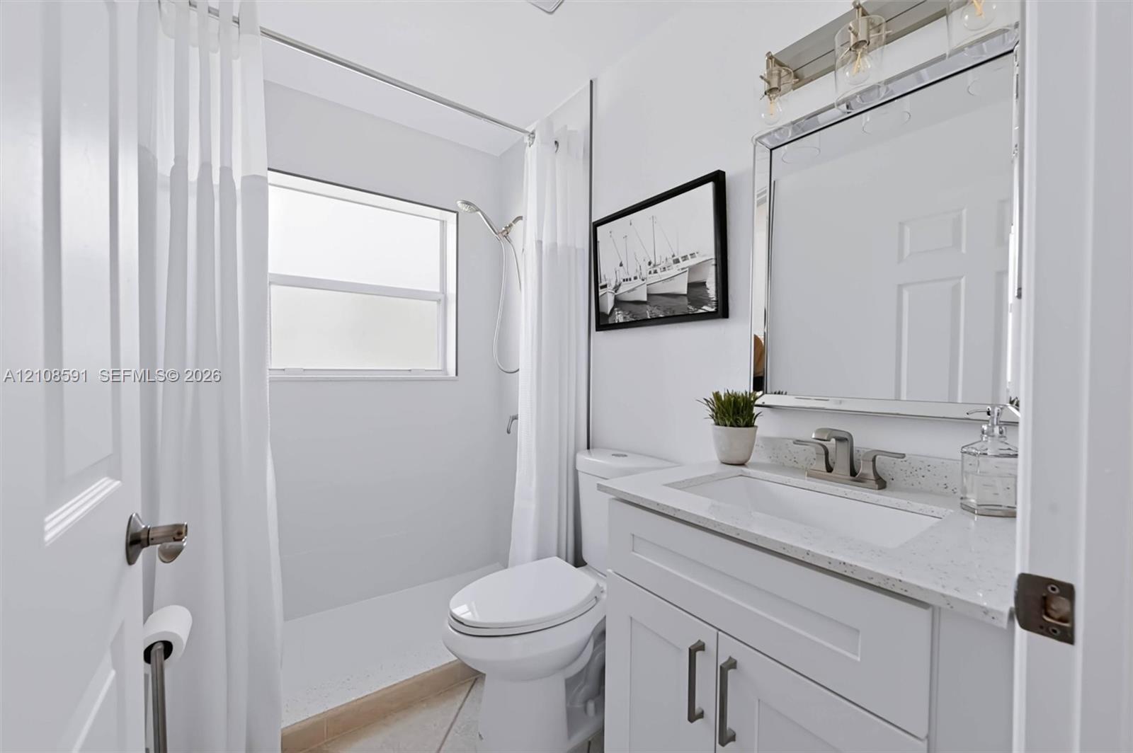 Bathroom featuring a vanity with white cabinetry, a light-toned stone countertop, an integrated rectangular sink, a framed mirror with integrated lighting, and a shower with a handheld fixture