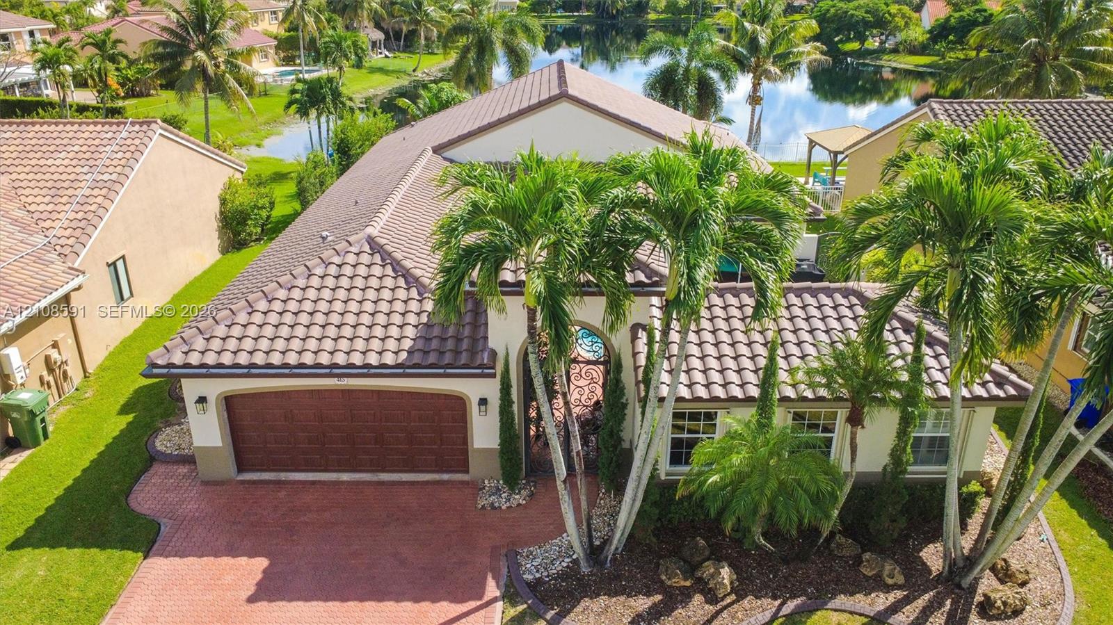 Single-story residence featuring a tile roof, brick-paver driveway, arched entryway, and waterfront location with established palm landscaping