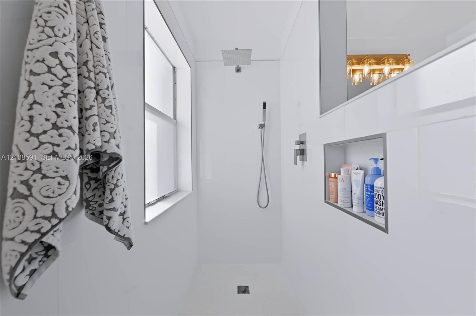 Walk-in shower featuring white wall panels, a square rainfall showerhead, a separate handheld sprayer, and a built-in recessed storage niche
