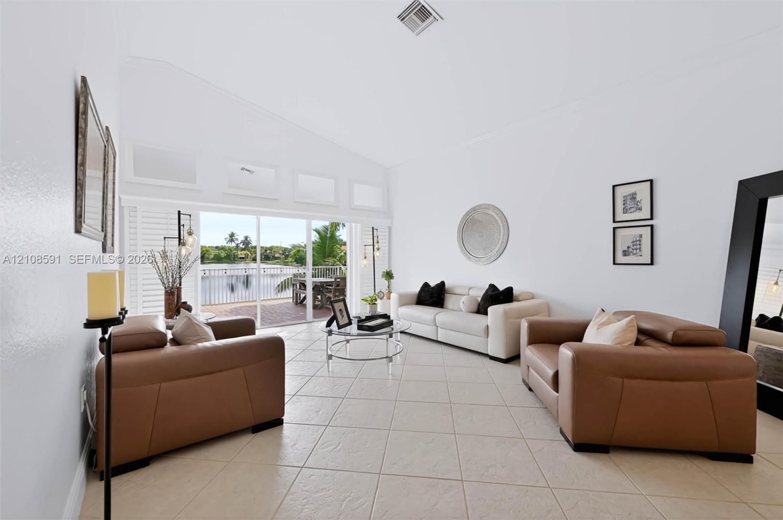 Living area featuring vaulted ceilings, oversized tile flooring, clerestory windows, and sliding glass doors opening to a waterfront balcony