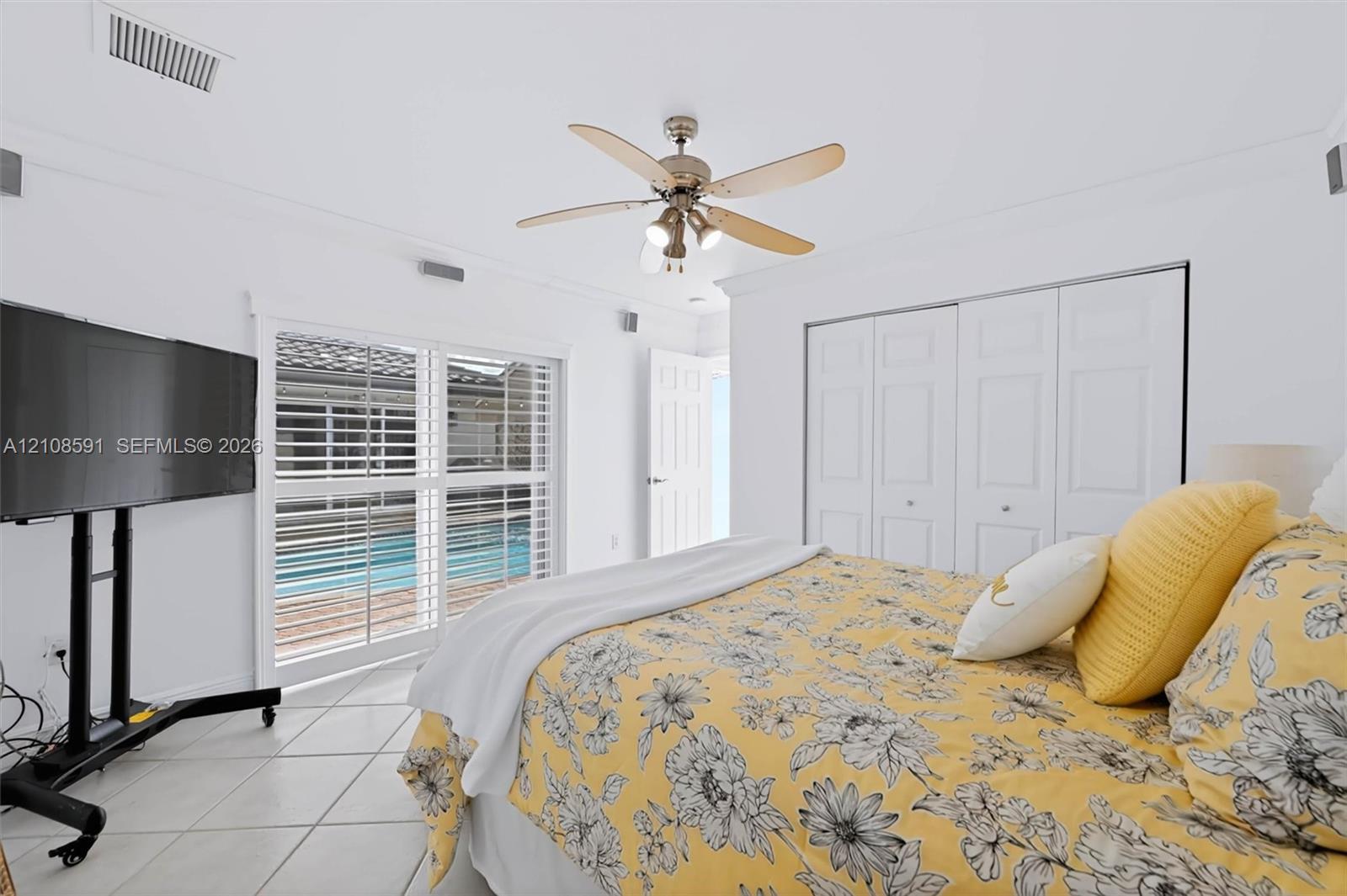 Interior featuring tile flooring, ceiling fan with integrated lighting, multi-panel closet doors, and sliding glass doors with plantation shutters