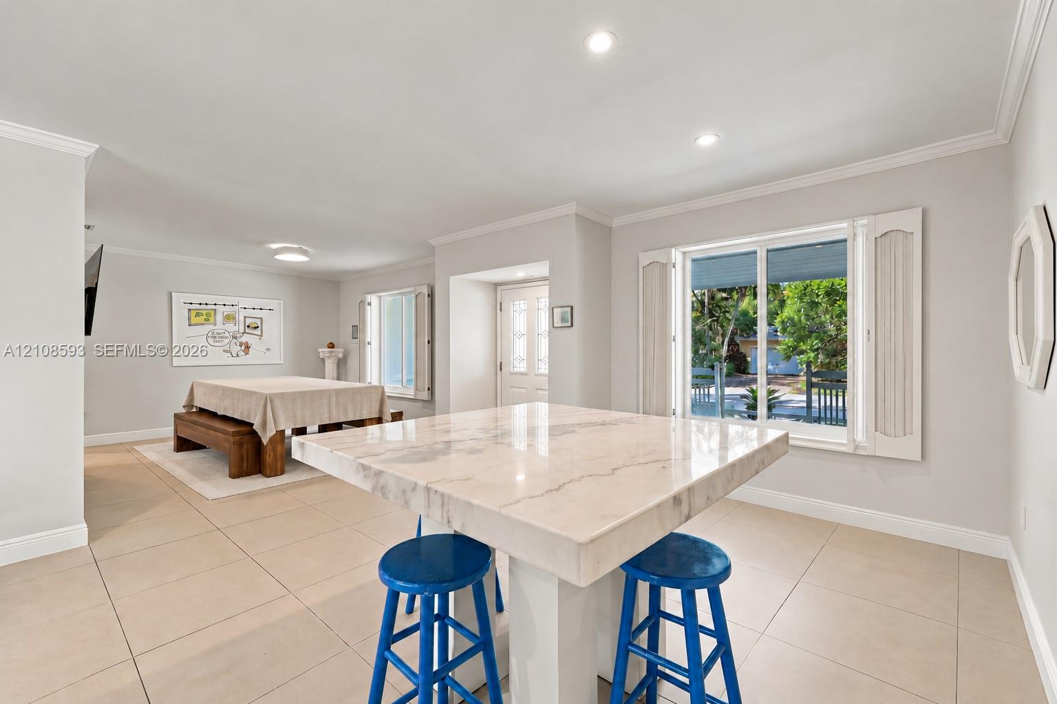 Open-concept interior featuring large-format tile flooring, recessed ceiling lighting, a central stone-top island, and dual windows equipped with plantation shutters Open-concept interior featuring large-format tile flooring, recessed ceiling lighting, a central stone-top island, and dual windows equipped with plantation shutters
