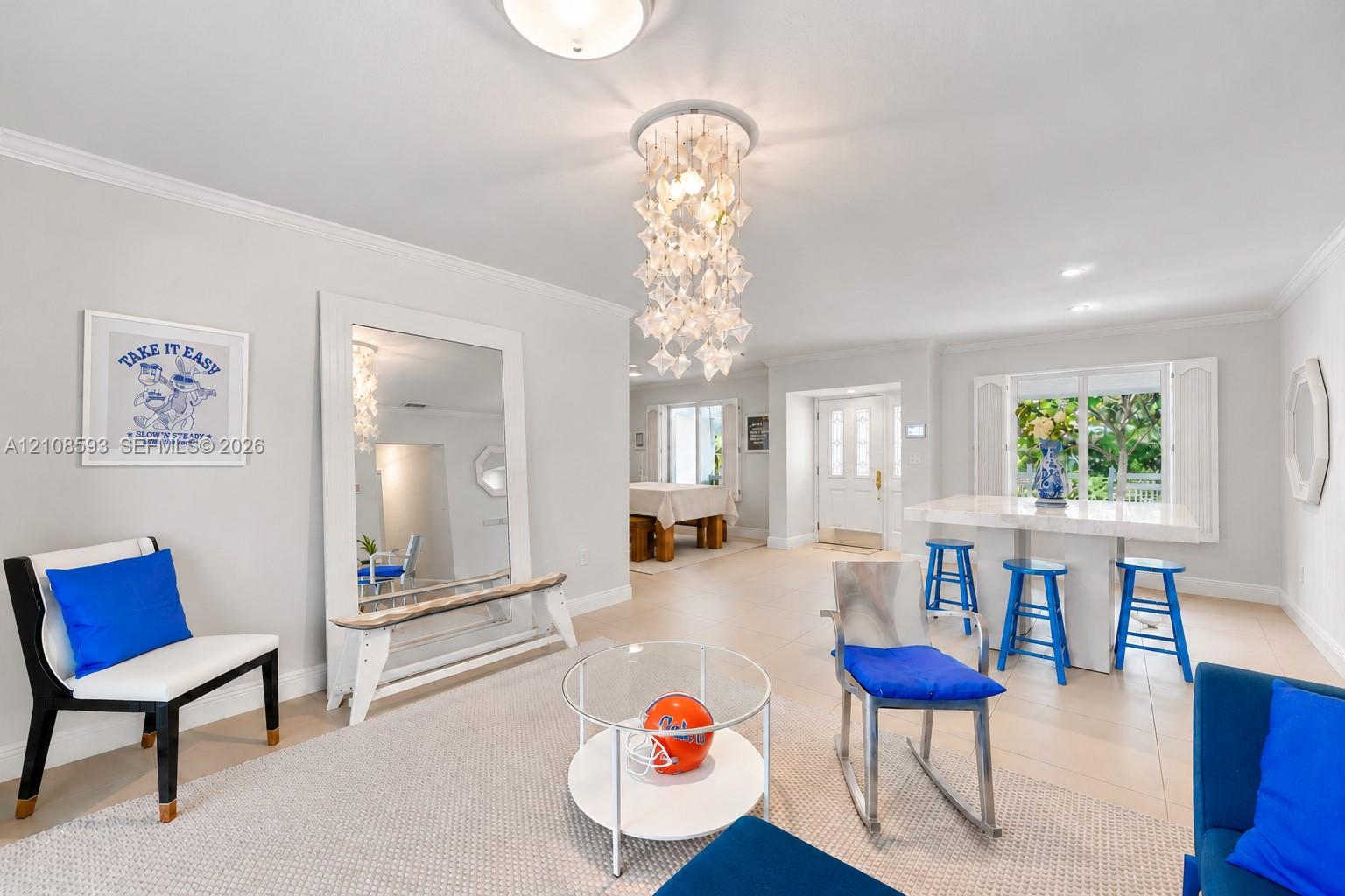 Open-concept interior featuring large-format tile flooring, a multi-tiered crystal-style chandelier, decorative crown molding, and a built-in stone-top island