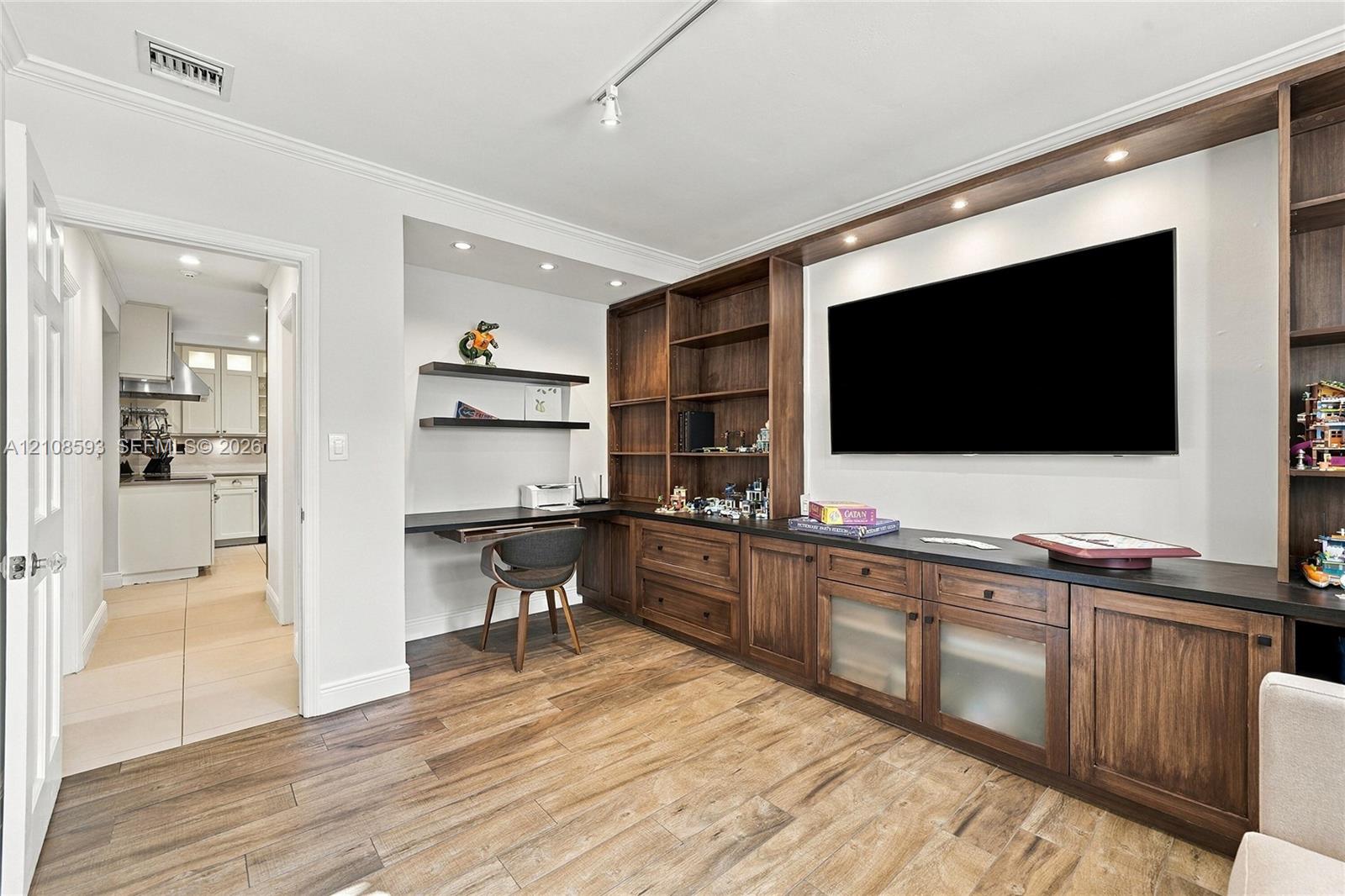 Custom built-in wood cabinetry with integrated shelving and drawers, dark countertop, recessed lighting, and wood-finish flooring