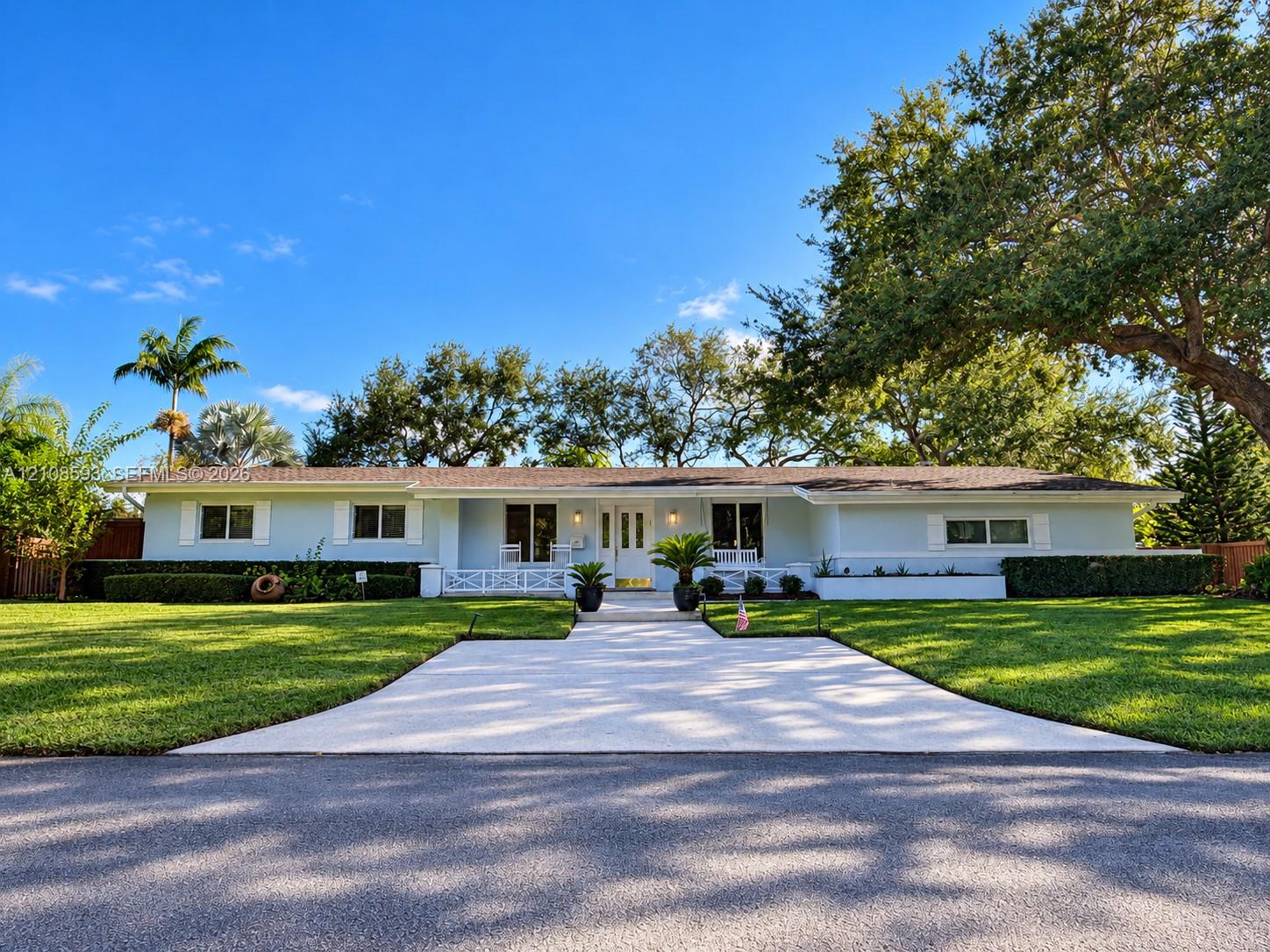 Single-story residence featuring light-toned exterior cladding, a paved walkway, covered front porch with decorative railing, and manicured landscaping